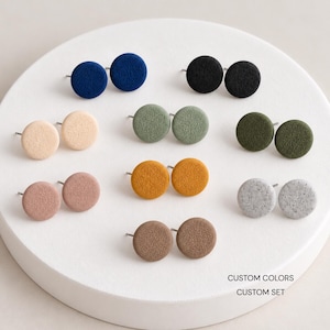 May include: A collection of nine pairs of circular stud earrings in various solid colors including navy, black, beige, sage green, olive green, dusty rose, mustard yellow, light gray, and brown, with the text CUSTOM COLORS CUSTOM SET.