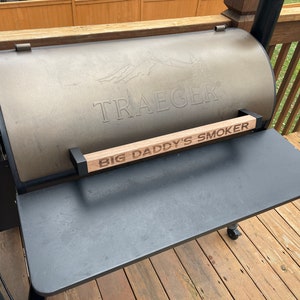 May include: A black Traeger grill with a wooden handle that says "Big Daddy's Smoker".