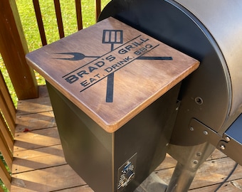 May include: A wooden lid for a black smoker grill with the text "Brad's Grill Eat, Drink, BBQ" and a grill utensil graphic.