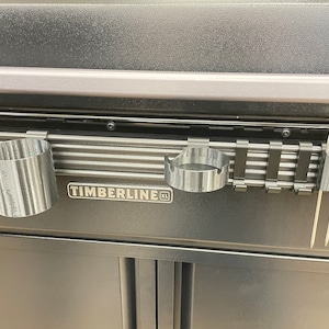 Könnte beinhalten: Ein schwarzer Grill mit einem silbernen Metallrost und zwei silbernen Getränkehaltern. Der Grill trägt den Schriftzug "TIMBERLINE XL" auf der Vorderseite.
