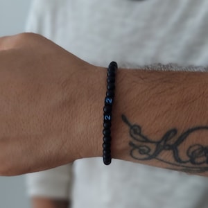 Può includere: Un braccialetto di perline nere con '2' blu su ogni perla.