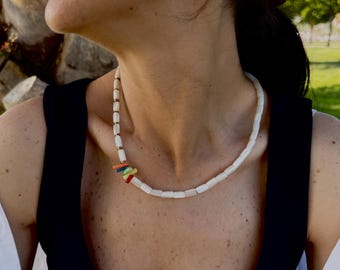 May include: A white beaded necklace with a colorful accent. The necklace features rectangular white beads and a section of small, colorful beads in orange, green, and blue. The necklace is worn against a black top.