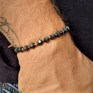 May include: A black beaded bracelet with gold accents. The bracelet is made of small, square-shaped beads.