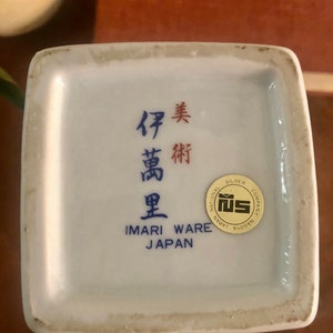 May include: A white Imari Ware ceramic piece with blue and red Japanese characters and the text "IMARI WARE JAPAN". A gold and white sticker reads "NATIONAL SILVER COMPANY NAGOYA".