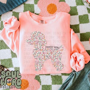 Pode incluir: Uma camisa de moletom rosa com uma silhueta de poodle floral e o texto "POODLE MOM" impresso nela.