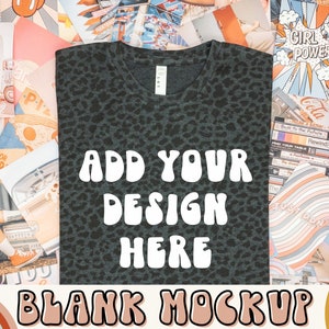 Könnte beinhalten: Ein schwarzes und graues T-Shirt mit Leopardenmuster und dem Text "ADD YOUR DESIGN HERE" in Weiß. Das Shirt liegt auf einem Tisch mit verschiedenen bunten Hintergründen und Mustern.