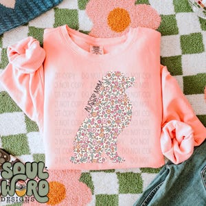May include: A pink sweatshirt with a floral pattern in the shape of an Australian Shepherd dog. The text "Aussie Mom" is printed on the sweatshirt.