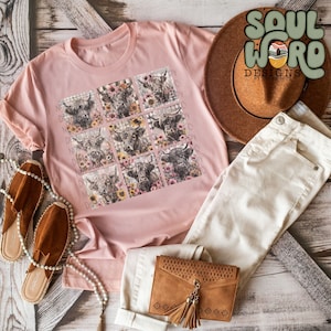 May include: A pink t-shirt with a graphic print of nine Highland cow faces surrounded by flowers. The cows are in a grid pattern and the flowers are in a variety of colors. The shirt is laying on a wooden surface with a pair of brown sandals, a brown purse, and a pair of white jeans.