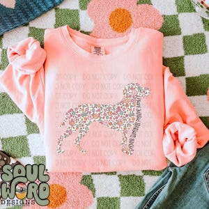 以下が含まれることがあります： 花柄の犬のシルエットと「German Shorthaired Pointer Mom」というテキストがプリントされたピンク色のスウェットシャツです。