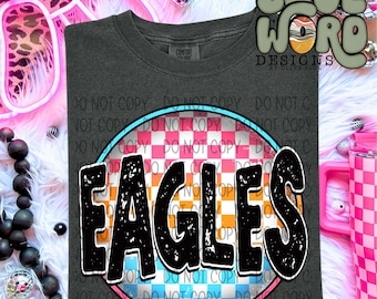 Puede incluir: Una camiseta gris oscura con un diseño circular que presenta la palabra "EAGLES" en negro con un aspecto desgastado. El círculo tiene un patrón a cuadros en rosa, azul, blanco y naranja.
