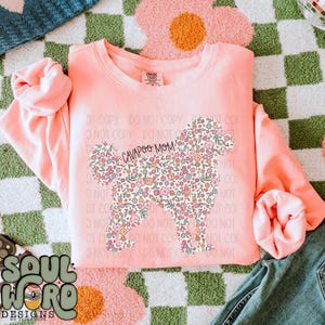 May include: A pink sweatshirt with a floral design of a cavapoo dog. The text "CAVAPOO MOM" is printed on the dog's body.
