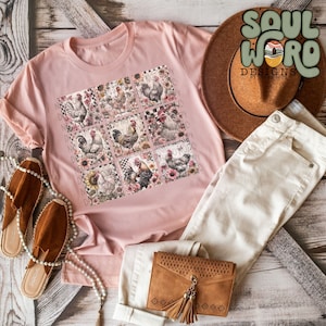 May include: A pink t-shirt featuring a graphic of nine square images of roosters and floral designs. The shirt is laid out on a wooden surface with a brown hat, white jeans, a brown purse, and brown sandals.