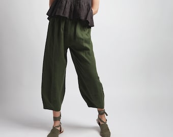 May include: A woman is wearing a black linen top with a ruffle hem and olive green linen pants. She is wearing olive green sandals.