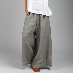 Könnte beinhalten: Ein ärmelloses Oberteil aus weißem Leinen und eine weite Hose mit vertikalen Streifen in Grau und Weiß. Das Outfit wird durch braune Lederschuhe ergänzt. Die Hose ist etwa 100 cm lang. Die Kleidung ist lässig.