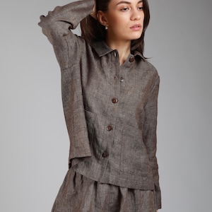 Può includere: Una camicia di lino marrone con colletto e maniche lunghe. La camicia ha una chiusura con bottoni sul davanti e due tasche a toppa.