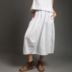 May include: A white linen skirt with a gathered waist and pockets. The skirt is midi length and has a relaxed fit.