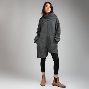 Peut inclure: Un pull long gris surdimensionné avec un col haut plié et des poches. Le pull est porté avec un legging noir et des bottines marron.