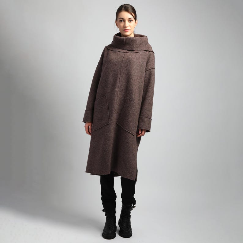 Woman wearing a long heavy boiled wool maxi coat in chestnut brown, featuring oversized pockets and a high funnel neckline, photographed on a neutral background.