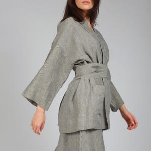May include: A gray and white striped linen jacket with a self-tie belt. The jacket has a relaxed fit and long sleeves.