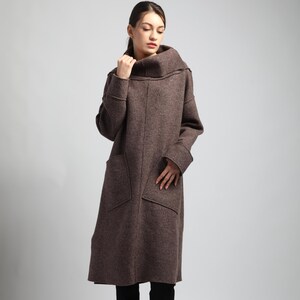 Puede incluir: Un abrigo largo de lana marr&oacute;n con un gran cuello alto y dos bolsillos delanteros. El abrigo tiene mangas largas y un dobladillo a la altura de la rodilla. El abrigo es de tejido suave y texturizado.