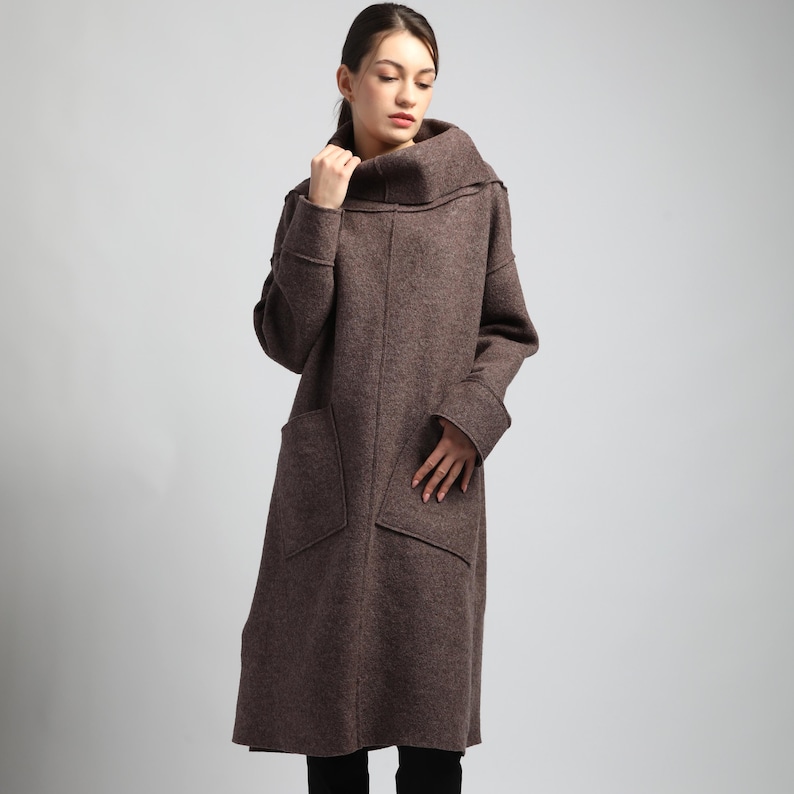 Puede incluir: Un abrigo largo de lana marr&oacute;n con un gran cuello alto y dos bolsillos delanteros. El abrigo tiene mangas largas y un dobladillo a la altura de la rodilla. El abrigo es de tejido suave y texturizado.