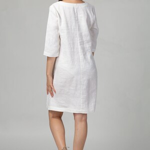 May include: A white linen dress with a scoop neck and three-quarter sleeves. The dress is knee-length and has a relaxed fit.
