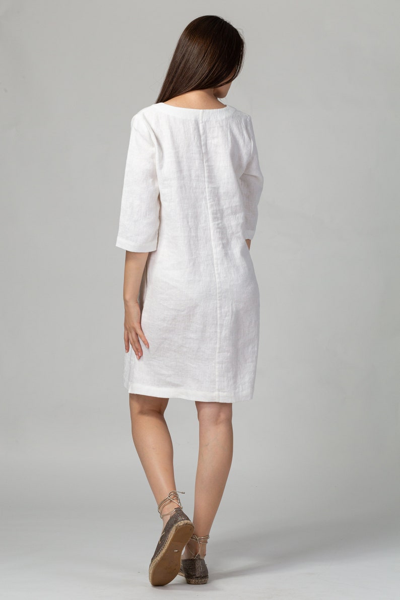 May include: A white linen dress with a scoop neck and three-quarter sleeves. The dress is knee-length and has a relaxed fit.