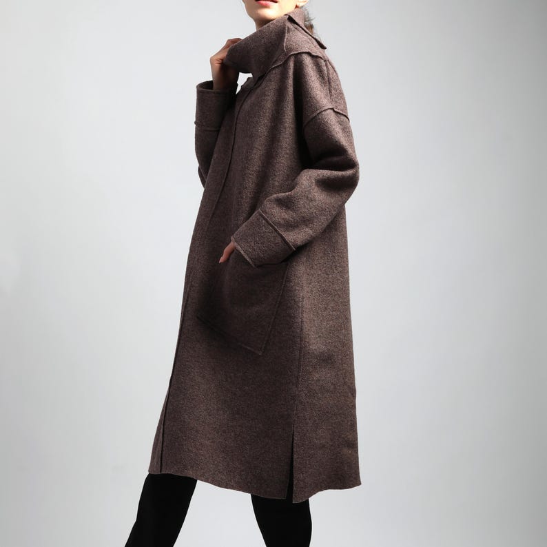 Puede incluir: Un abrigo largo marr&oacute;n con cuello alto y bolsillos grandes. El abrigo est&aacute; hecho de una tela texturizada y tiene un ajuste relajado. El abrigo se usa sobre pantalones negros.