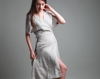 May include: A woman wearing a light beige linen wrap dress with a short sleeve and a tie at the waist.