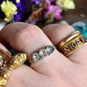 May include: A silver ring with five round, clear gemstones set in a row. The ring is on a person's finger.