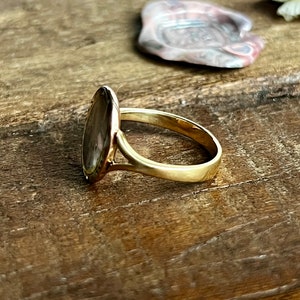 May include: A gold ring featuring a large oval-shaped stone set in the centre. The stone has a brown and white marbled pattern.