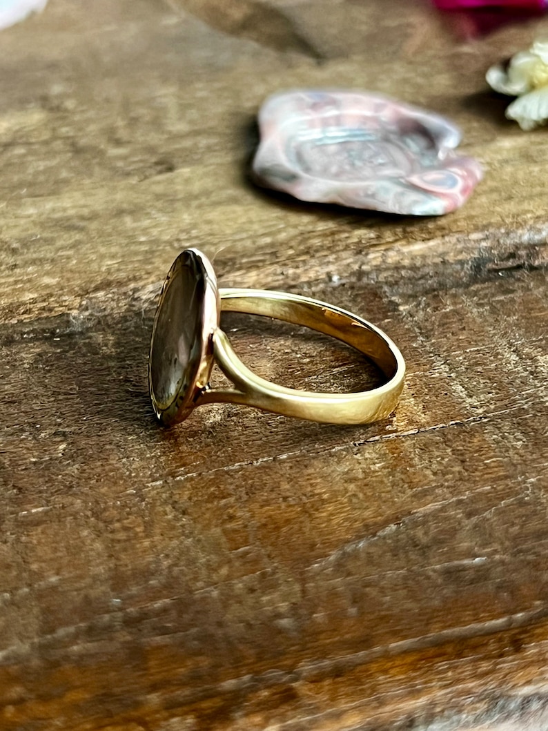 May include: A gold ring featuring a large oval-shaped stone set in the centre. The stone has a brown and white marbled pattern.