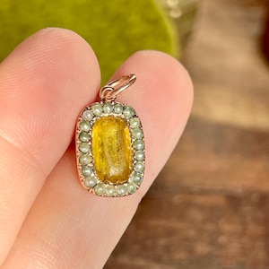 May include: A gold pendant with a yellow gemstone surrounded by a border of small white pearls.