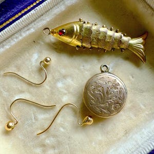 Puede incluir: Conjunto de joyería de oro vintage, que incluye un broche con forma de pez con un ojo de gema roja, un colgante redondo con grabado floral y dos pares de pendientes de oro. Las piezas se exhiben en una caja forrada de terciopelo.