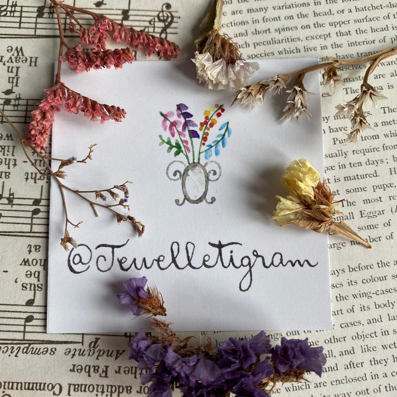 May include: A white card with a hand-drawn illustration of a vase with colourful flowers. The text "@Tevelletigram" is written in black ink below the illustration.