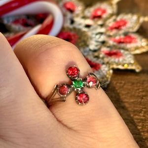 Puede incluir: Un anillo de plata con un diseño de cruz con cinco piedras preciosas rojas y una verde.