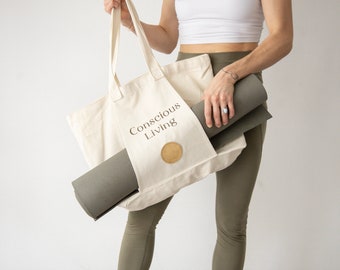 May include: A person carrying a beige canvas tote bag with the text "Conscious Living" printed on it. A grey yoga mat is tucked inside the bag.