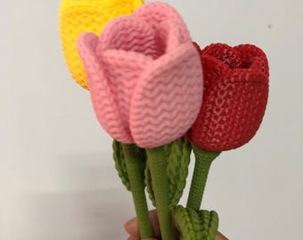 May include: Three handmade crochet tulips in vibrant colors: yellow, pink, and red. The flowers have green stems and leaves. The textured petals and detailed craftsmanship create a charming floral arrangement.