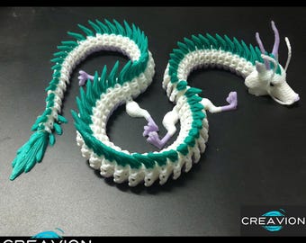 May include: A 3D-printed articulated dragon in white, teal, and lavender. The dragon has a long, winding body with teal spikes and a teal tail. The dragon's legs and head are lavender. The dragon is on a dark surface. The logo "CREAVION" is visible.