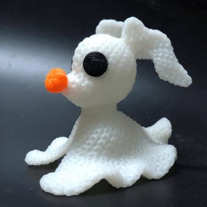 Może przedstawiać: Biała figurka psa ducha z pomarańczowym nosem i czarnymi oczami. Pies ma oklapnięte uszy i pofałdowany, przypominający spódnicę dół. Figurka jest postacią z filmu "Miasteczko Halloween".