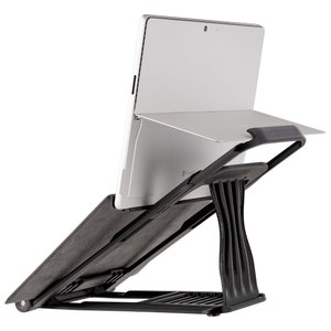 May include: A black laptop stand with a grey padded surface and a foldable design. The stand is angled to elevate a laptop or tablet.