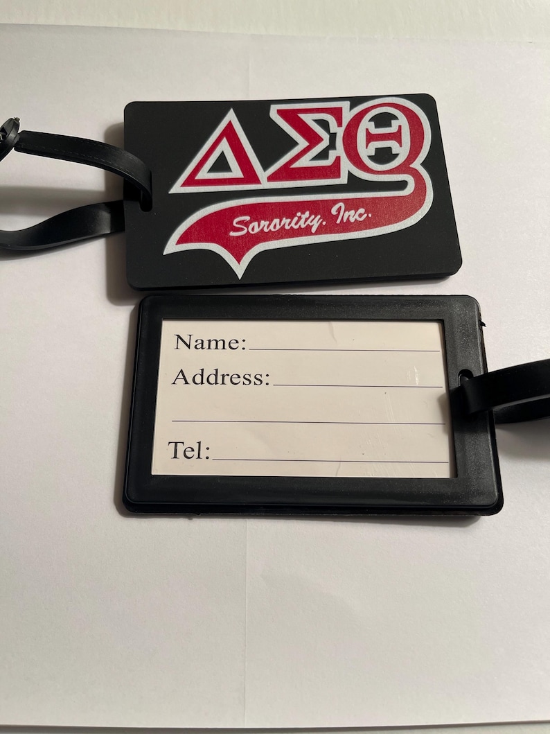 May include: Black luggage tag with a red and white Delta Sigma Theta Sorority, Inc. logo. The tag has a white label with spaces for a name, address, and telephone number.