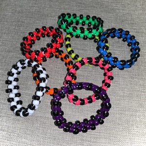 May include: A set of eight colorful kandi bracelets with black and white beads. The bracelets are made of plastic and are approximately 7 inches in circumference.