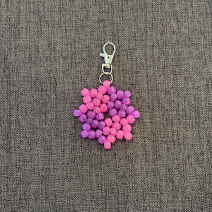 May include: A pink and purple beaded keychain in the shape of a flower with a silver metal key ring.