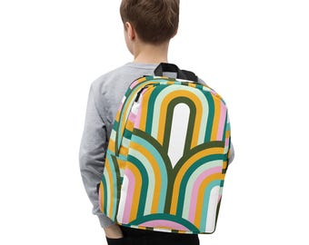 May include: A colorful backpack with a retro rainbow pattern in shades of green, yellow, pink, and blue. The backpack has a black top handle and zipper. The bag is worn by a person in a gray long-sleeve shirt.