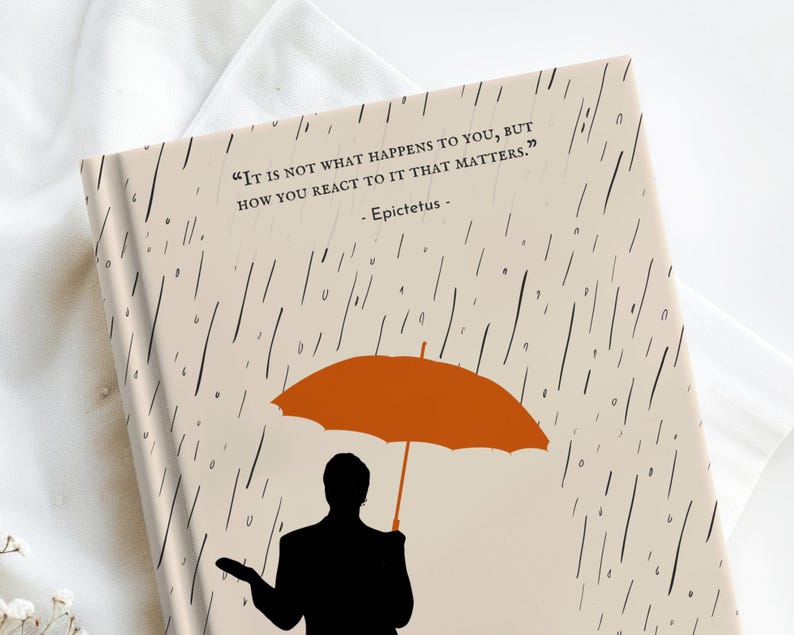 May include: A beige journal with a black and white rain pattern and a quote by Epictetus: "It is not what happens to you, but how you react to it that matters." A silhouette of a person holding an orange umbrella is in the lower right corner.