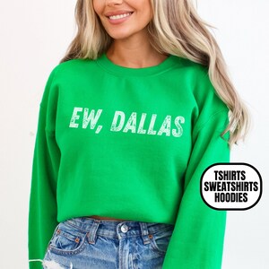 May include: A bright green sweatshirt with the phrase "EW, DALLAS" printed in white. The sweatshirt has long sleeves and a crew neck. The image also includes text that says "TSHIRTS SWEATSHIRTS HOODIES" and "IRISH GREEN".