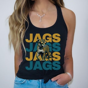 May include: A black racerback tank top featuring a graphic of a leopard wearing sunglasses. The text JAGS is printed in alternating gold and teal rows behind the leopard. The tank top has a knotted hem at the waist and a scoop neckline.