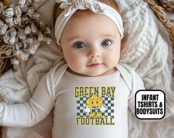 May include: A white long-sleeve bodysuit featuring a graphic of a cartoon cheese wedge with the text GREEN BAY FOOTBALL above and below a checkered pattern. The garment includes a white floral headband and a light pink tulle skirt overlay.