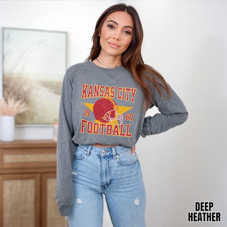 May include: A gray long-sleeved shirt with a vintage-style graphic of a football helmet and the text "Kansas City Football" with the numbers 19 and 60 on either side of the helmet.